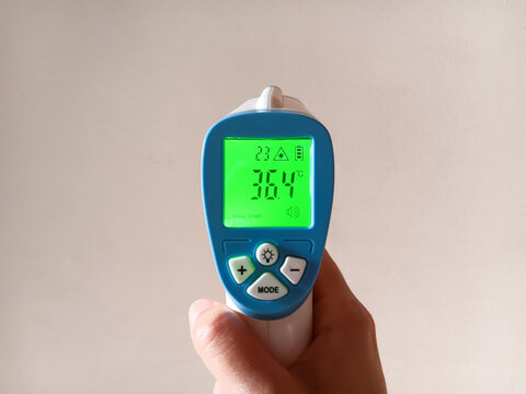 Woman hand showing infrared (IR) digital thermometer gun with normal body temperature isolated in white background.