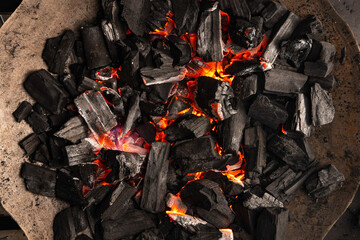 Hot coals with vibrant red and orange hues, emitting intense heat. Glowing pieces surrounded by dark ash, creating a rustic atmosphere