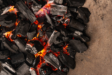 Hot coals with vibrant red and orange hues, emitting intense heat. Glowing pieces surrounded by dark ash, creating a rustic atmosphere