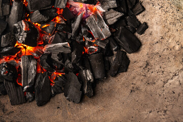 Hot coals with vibrant red and orange hues, emitting intense heat. Glowing pieces surrounded by dark ash, creating a rustic atmosphere