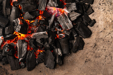 Hot coals with vibrant red and orange hues, emitting intense heat. Glowing pieces surrounded by dark ash, creating a rustic atmosphere
