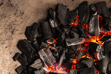 Hot coals with vibrant red and orange hues, emitting intense heat. Glowing pieces surrounded by dark ash, creating a rustic atmosphere