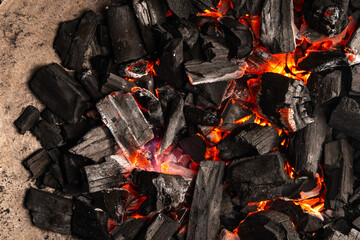 Hot coals with vibrant red and orange hues, emitting intense heat. Glowing pieces surrounded by dark ash, creating a rustic atmosphere