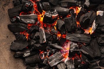 Hot coals with vibrant red and orange hues, emitting intense heat. Glowing pieces surrounded by dark ash, creating a rustic atmosphere