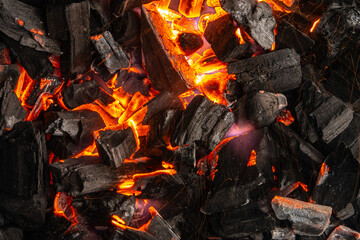 Hot coals with vibrant red and orange hues, emitting intense heat. Glowing pieces surrounded by dark ash, creating a rustic atmosphere
