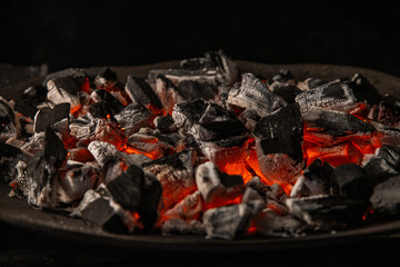 Hot coals with vibrant red and orange hues, emitting intense heat. Glowing pieces surrounded by dark ash, creating a rustic atmosphere