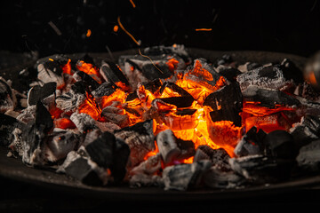 Hot coals with vibrant red and orange hues, emitting intense heat. Glowing pieces surrounded by dark ash, creating a rustic atmosphere