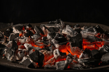 Hot coals with vibrant red and orange hues, emitting intense heat. Glowing pieces surrounded by dark ash, creating a rustic atmosphere