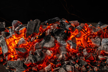 Hot coals with vibrant red and orange hues, emitting intense heat. Glowing pieces surrounded by dark ash, creating a rustic atmosphere