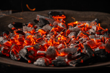 Hot coals with vibrant red and orange hues, emitting intense heat. Glowing pieces surrounded by dark ash, creating a rustic atmosphere
