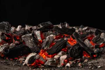Hot coals with vibrant red and orange hues, emitting intense heat. Glowing pieces surrounded by dark ash, creating a rustic atmosphere