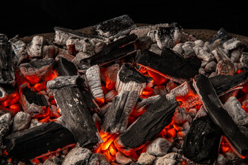 Hot coals with vibrant red and orange hues, emitting intense heat. Glowing pieces surrounded by dark ash, creating a rustic atmosphere
