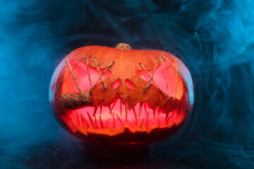 Halloween pumpkin with sharp, needle-like teeth and eyes sewn shut with thick strings, glowing from within against a black background, enveloped in smoke