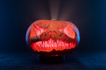 Halloween pumpkin with sharp, needle-like teeth and eyes sewn shut with thick strings, glowing from...