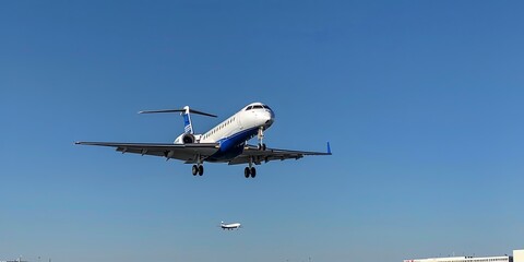 Fototapeta premium A white and blue commercial airplane approaches the runway for landing against a clear blue sky.