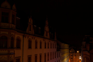 Naklejka premium A long row of buildings stands out brightly illuminated at night in a dark city, creating a striking contrast against the night sky