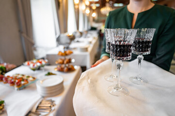 A waiter elegantly serves red wine at a banquet, with a blurred background of appetizers and guests, capturing the essence of fine dining and hospitality. Perfect for illustrating upscale restaurant