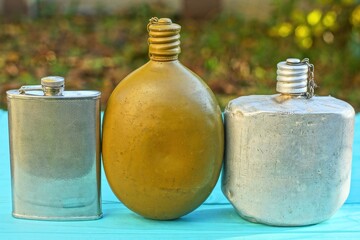 three different army closed empty old retro round aluminum with lid on chain military soldier two gray and green dirty with cup hiking industrial flasks lie on a green wooden table