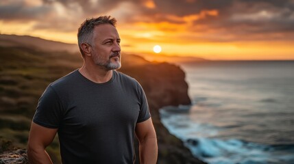 A middle-aged man watches the sunrise at a cliff's edge, taking in the peaceful ocean landscape - Powered by Adobe