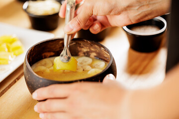 The chef's hands preparing a bowl of fruit smoothie, he is placing mango on top. Woman preparing healthy breakfasts and snacks for children, mothers, pregnant women, athletes.