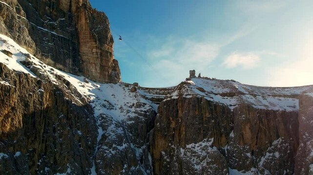 A cable car glides across a snow-covered mountain range in the dolomites under a clear blue sky, showcasing the rugged beauty of nature of Dolomiti Superski.