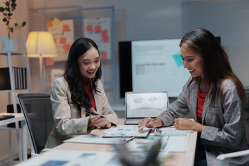 Two smiling businesswomen working late in the office, analyzing financial data and enjoying their teamwork