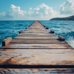 Obraz premium A long wooden pier stretches into the vast blue ocean under a sky with clouds, representing tranquility and adventure.