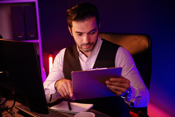 Stressful smart businessman analyzing market data on paper work report folder to create sales channel online of discipline's product service at purple neon dark light room at late night time. Surmise.