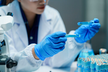 Scientist wearing a lab coat and safety glasses comparing two test tubes while working in a...