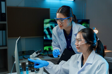 Two scientists wearing lab coats and safety glasses working together in a laboratory, analyzing data on a computer screen