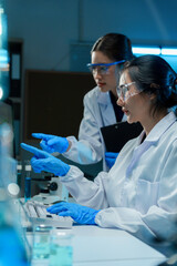 Two scientists wearing lab coats and safety glasses are working together in a laboratory, analyzing...