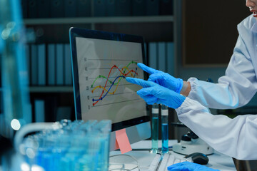 Two scientists wearing lab coats and gloves analyzing data displayed on a computer screen in a laboratory setting
