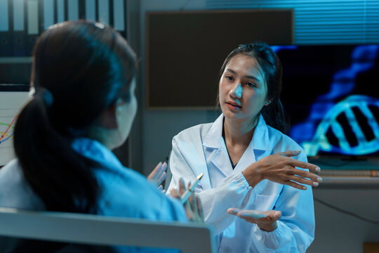 Two scientists are having a discussion about their research in a laboratory, with a dna double helix graphic displayed in the background