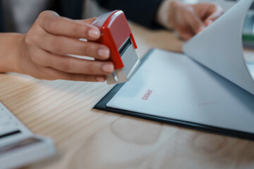 Close up view of businesswoman holding stamp in hand and stamping approved on document at office...