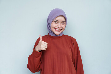 Happy young Asian Muslim woman wearing hijab with thumbs up gesture. Isolated white background.