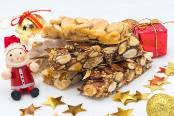 Different types of turrón (nougat), a traditional Christmas sweet in Spain, with some Christmas decoration ( a wooden Santa Claus, a gift box, a jingle bell and some stars), on a white background.