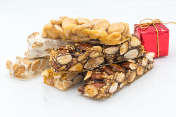 Different types of turrón (nougat), a traditional Christmas sweet in Spain, with some Christmas decoration ( a red Christmas gift), on a white background.