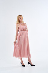 Woman in pink dress posing for photo. She is pregnant and wearing necklace. Mother love concept.