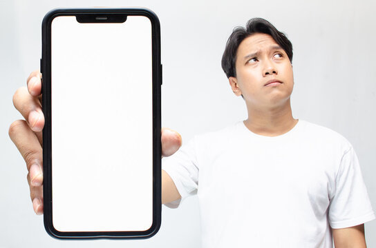 an overthinker young asian man thinking deeply while showing his big screen phone after receiving bad news. mock up of thoughtful asian man showing his blank screen phone