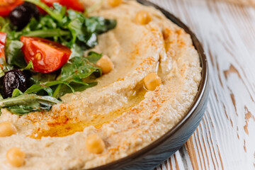 Creamy hummus close-up with fresh greens, cherry tomatoes, and chickpeas for healthy dining