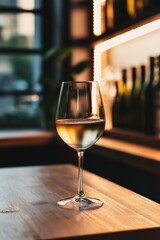A sleek wine glass with white wine sits on a sunlit table, creating a cozy atmosphere.