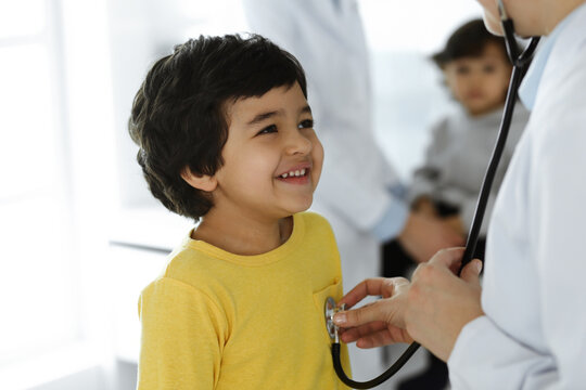 Woman-doctor examining a child patient by stethoscope. Cute arab boy at physician appointment. Medicine help concept