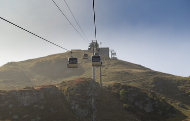 A group of cable cars are suspended over a green slope. Aerial tramway in Alps.