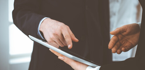 Businessman and woman using tablet computer for discussing questions in office. Partners or colleagues at meeting. Business cooperation concept