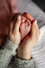 Close up mother gently holding and stroking newborn baby tiny foot in hands. Heartwarming moment, tenderness and care between mother and child, new life in soft, natural light