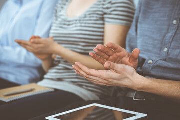 Obraz premium Business people clapping at meeting or conference, close-up of hands. Group of unknown businessmen and women in modern white office. Success teamwork, corporate coaching and applause concept