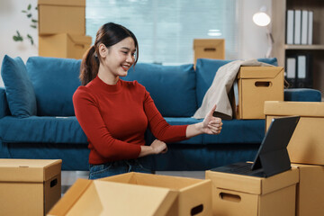 Young woman is giving a thumbs up gesture while having a video call in her new apartment, surrounded by cardboard boxes