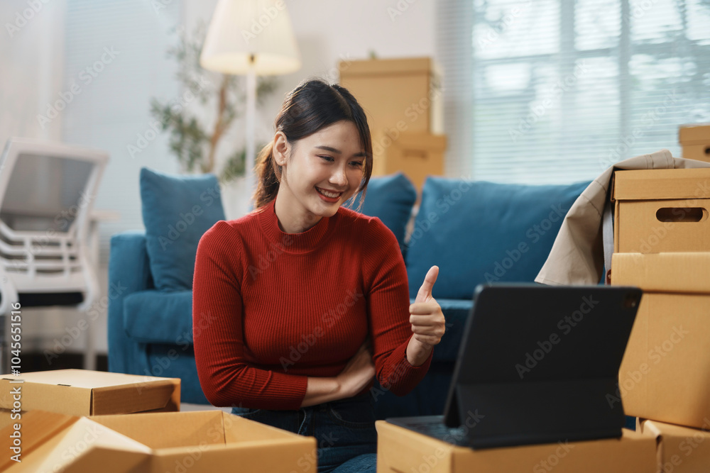 Wall mural young woman is giving a thumbs up gesture while having a video call on a tablet in her new apartment