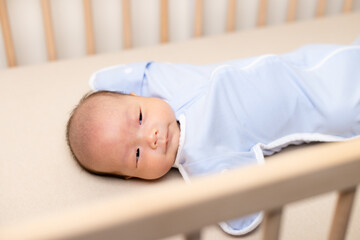 Asian newborn baby wear swaddle and lying on baby crib