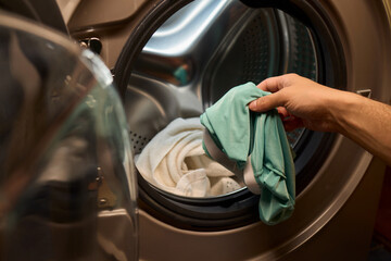 A person is loading various clothes into a washing machine to get them clean and fresh